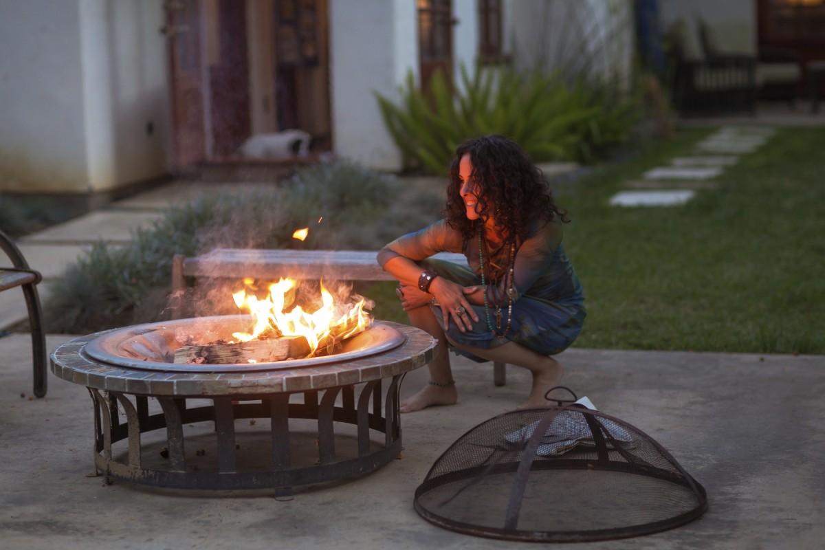 Woman crouching by fire pit in garden at dusk