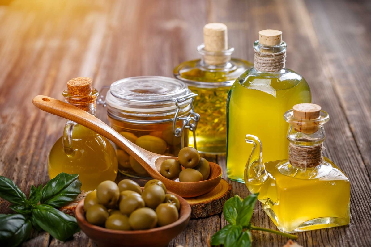 Variety of olive oil bottles with green olives and basil