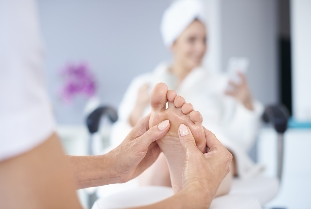 Woman receiving foot massage at spa with flowers visible.