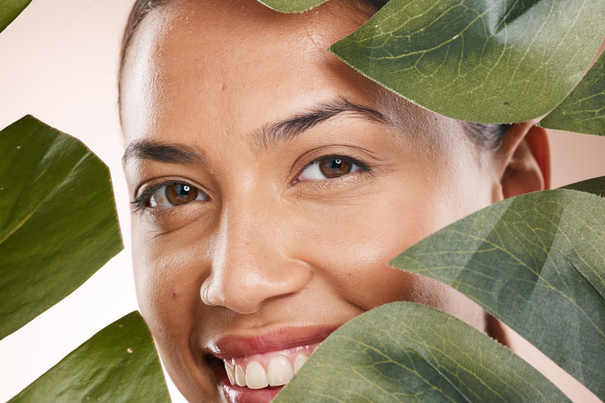 Woman smiling behind green leaves, close-up portrait