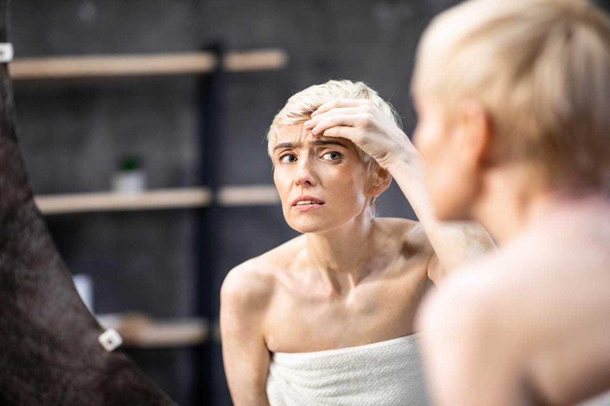 Concerned woman examining forehead in mirror