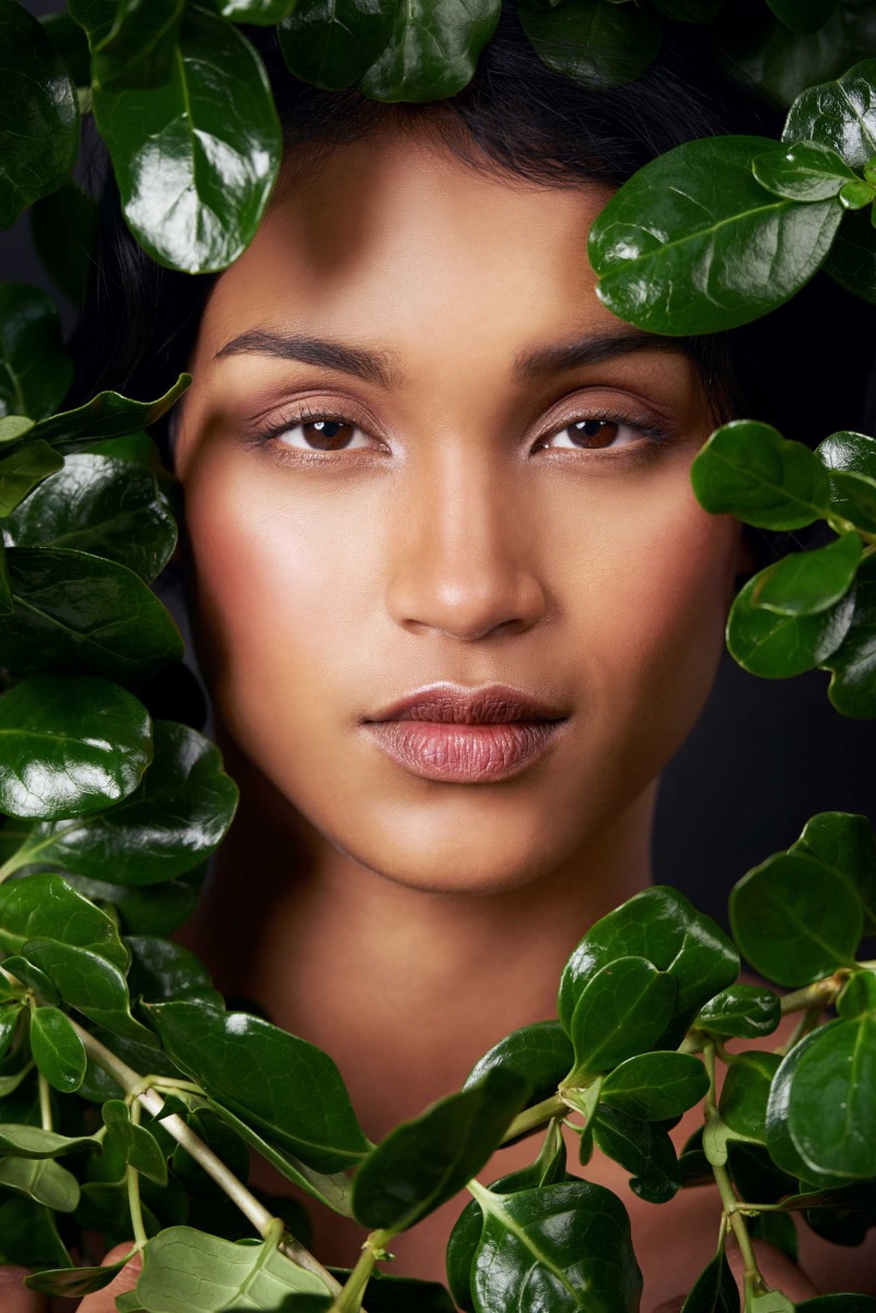 Woman surrounded by lush green leaves, close-up portrait