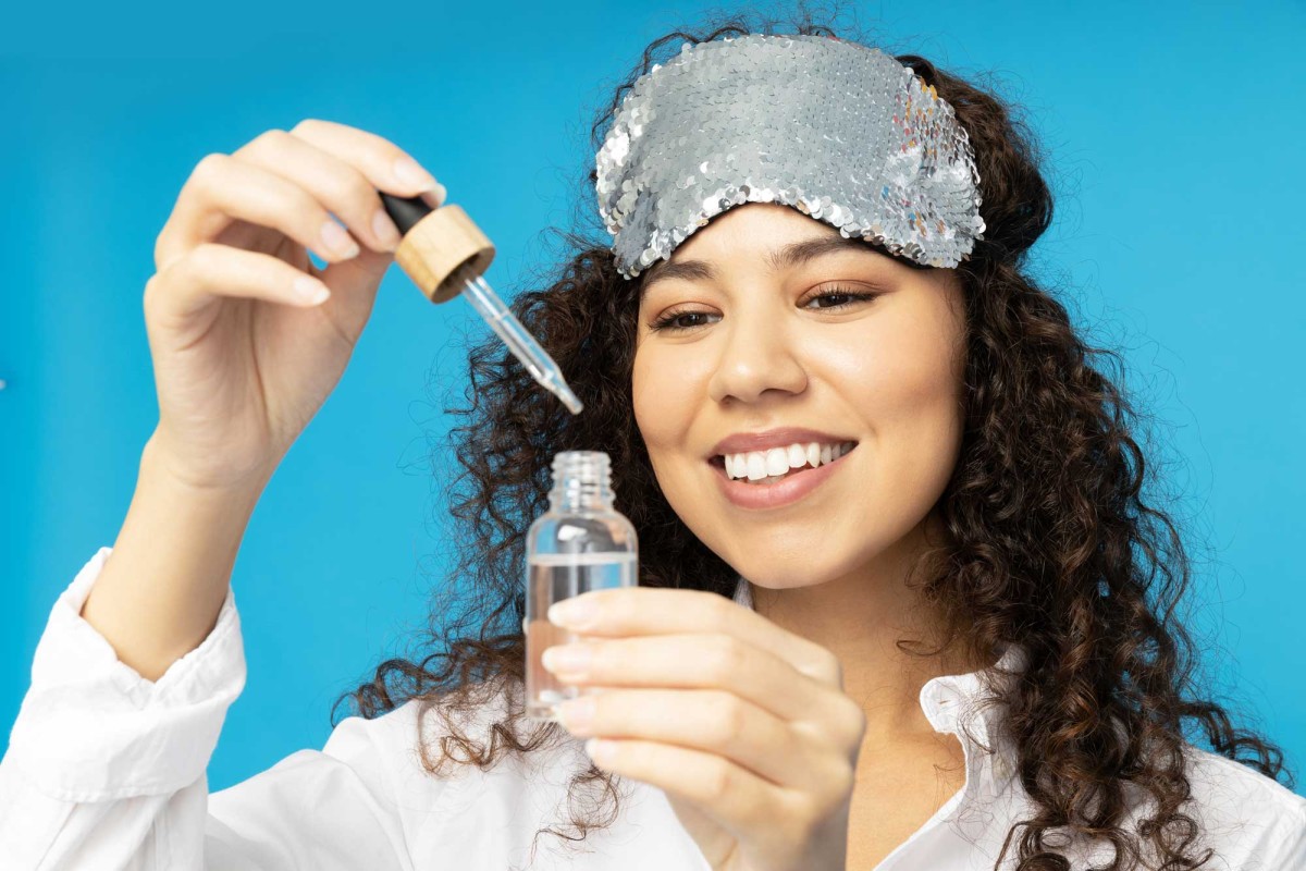 Woman applying serum with dropper, wearing sparkly headband