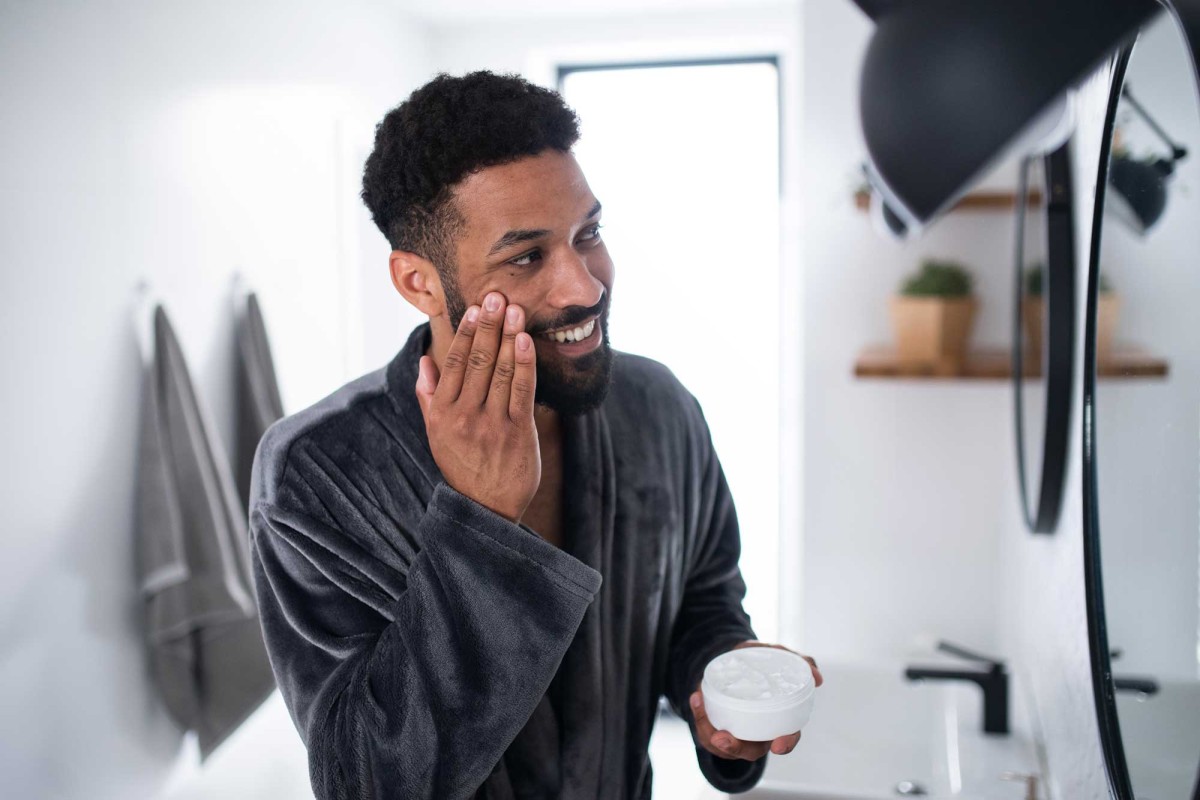 Man smiling, applying facial cream in bright bathroom