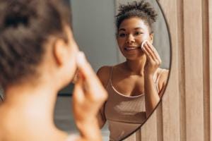 Woman smiling using cotton pad in mirror reflection