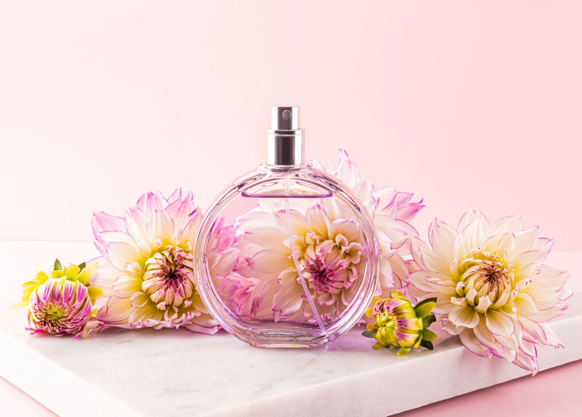 Perfume bottle surrounded by pink dahlias on marble