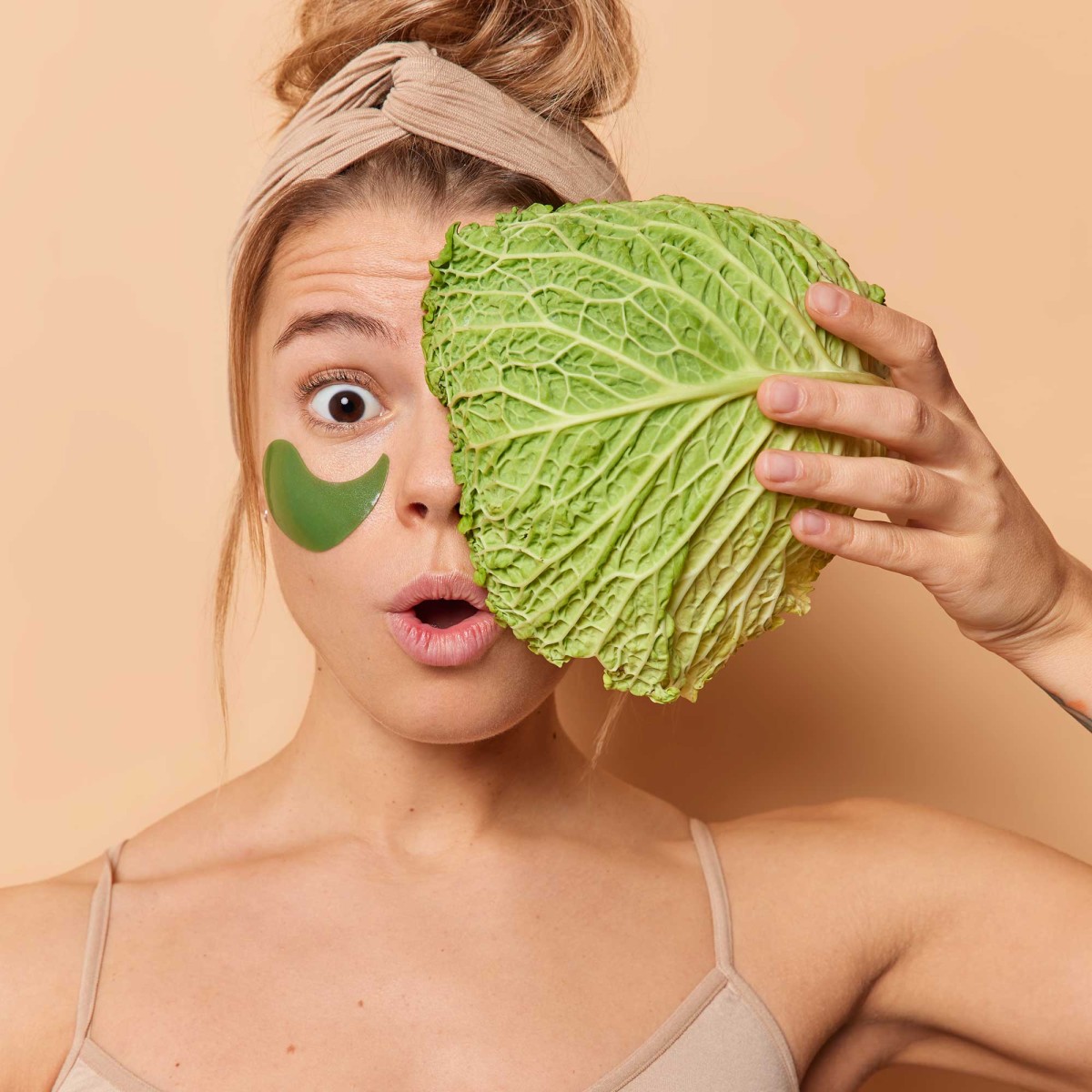 Woman covering eye with cabbage, skincare patch visible