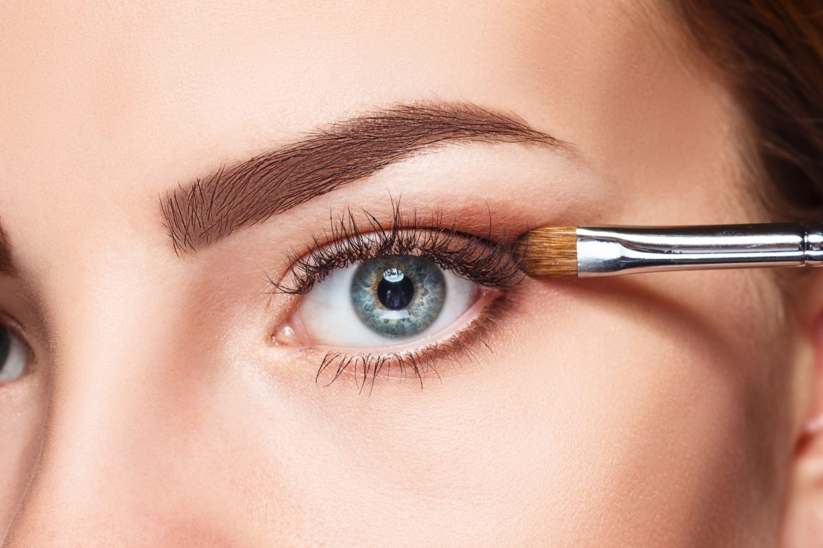 Applying eyeshadow on woman's blue eye close-up