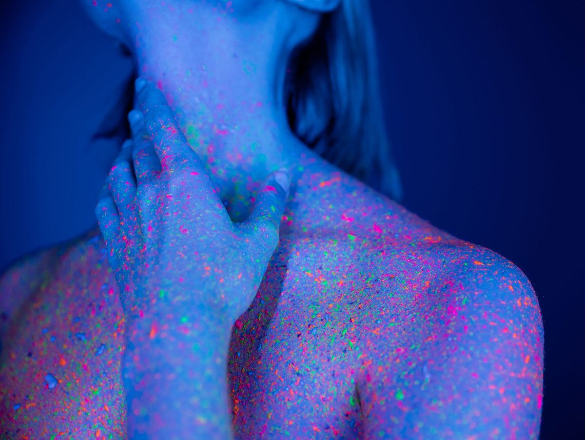 Person covered in colorful neon glitter under blue light