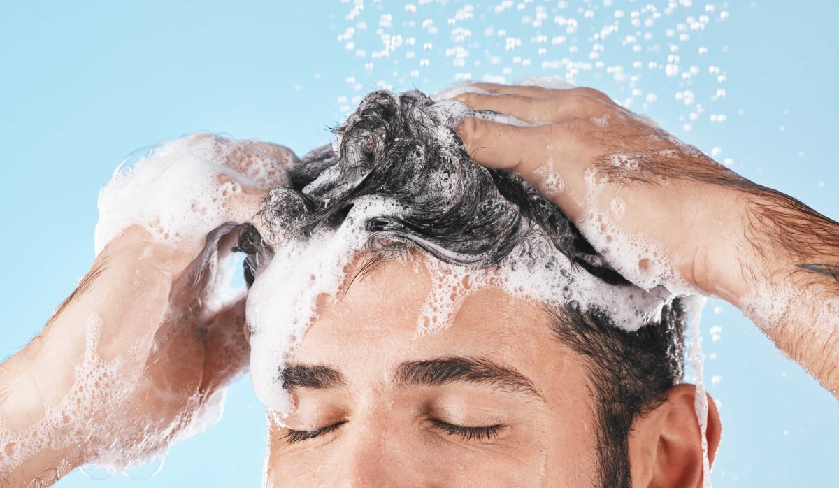 Man washing hair with shampoo, water droplets visible