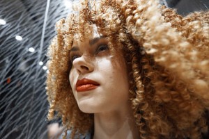 Woman with curly hair gazing upward, rain-like background