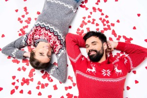 Couple in festive sweaters lying among red hearts