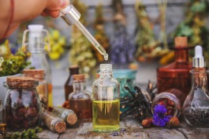 Essential oils with dried herbs on wooden table