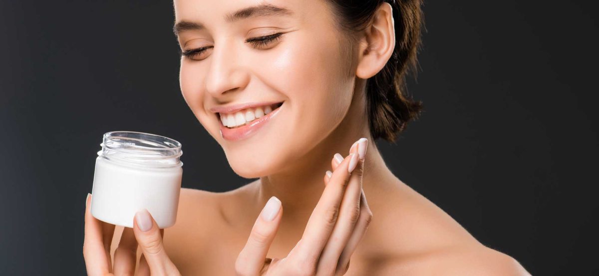 Woman applying moisturizer from jar, smiling