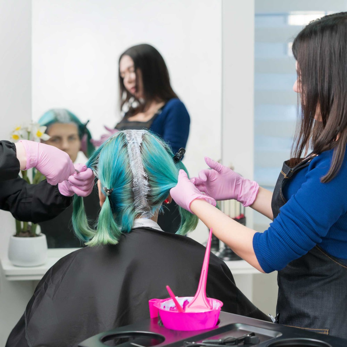 Hair stylist dyeing woman's hair blue in salon