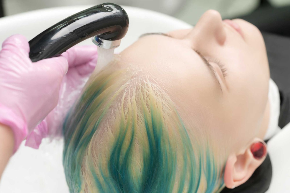 Hairdresser rinsing colored hair in salon sink