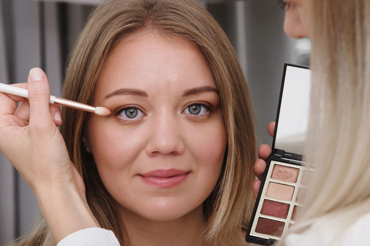 Woman applying eyeshadow in mirror with makeup brush