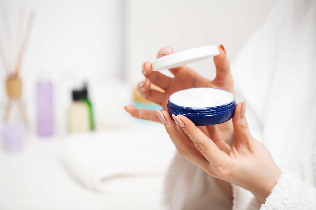 Woman holding open container of moisturizing cream