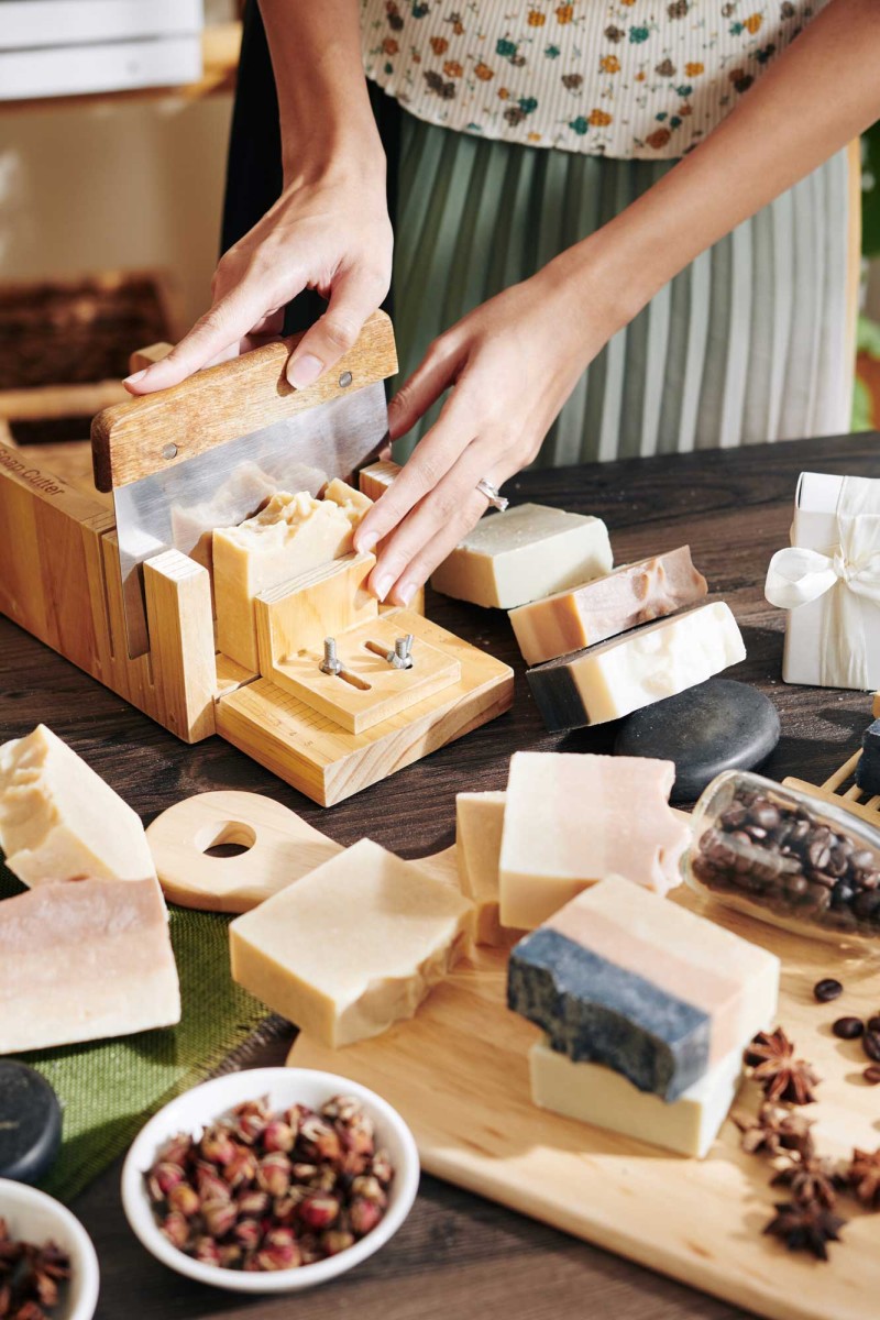 Person slicing handmade soap on wooden table