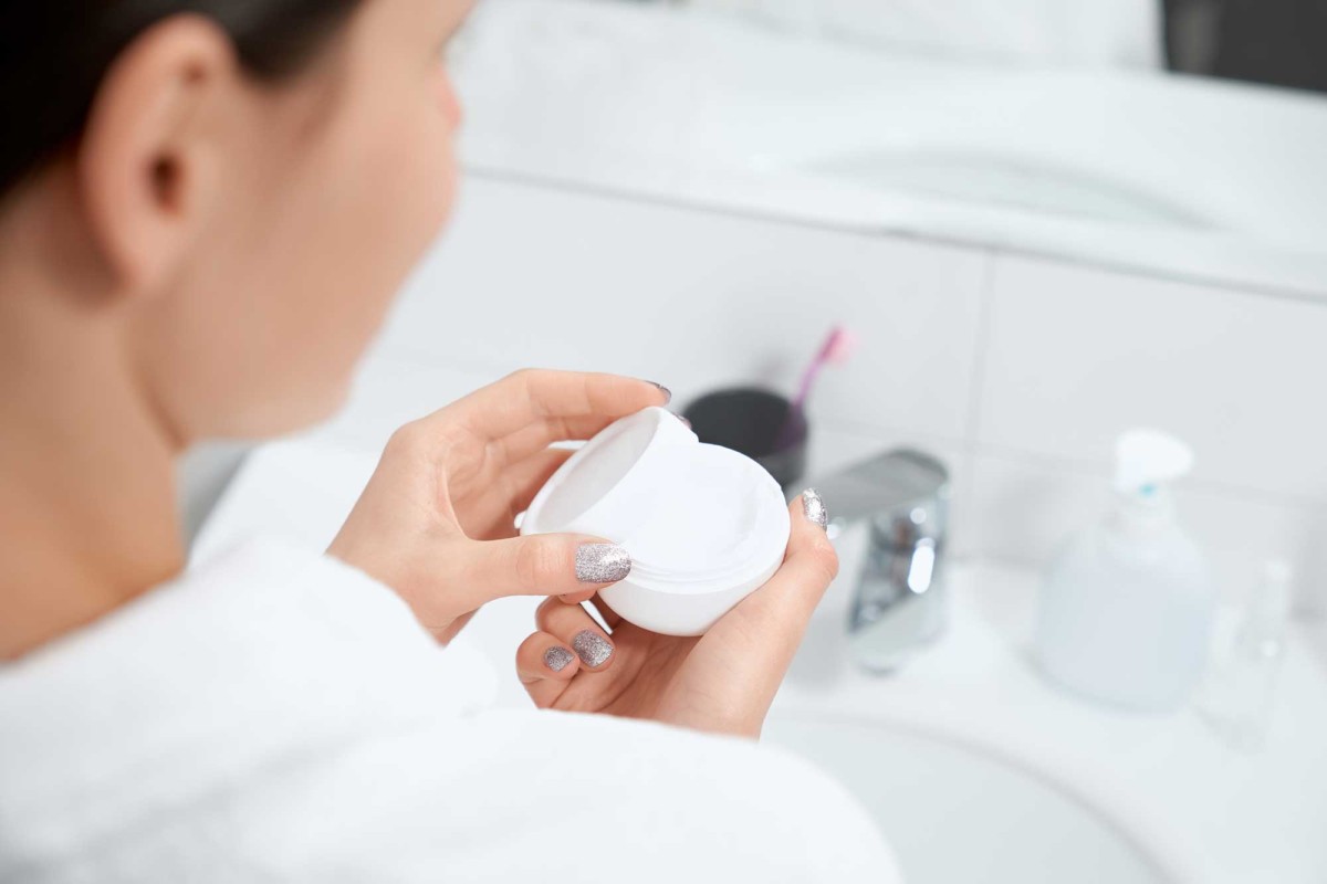 Woman holding open jar of face cream in bathroom