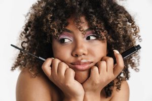 Woman applying mascara, thoughtful expression, white background