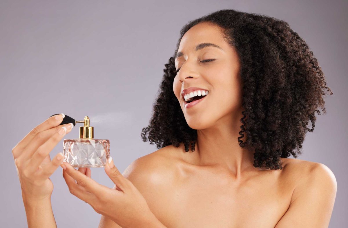 Happy woman applying perfume from ornate bottle