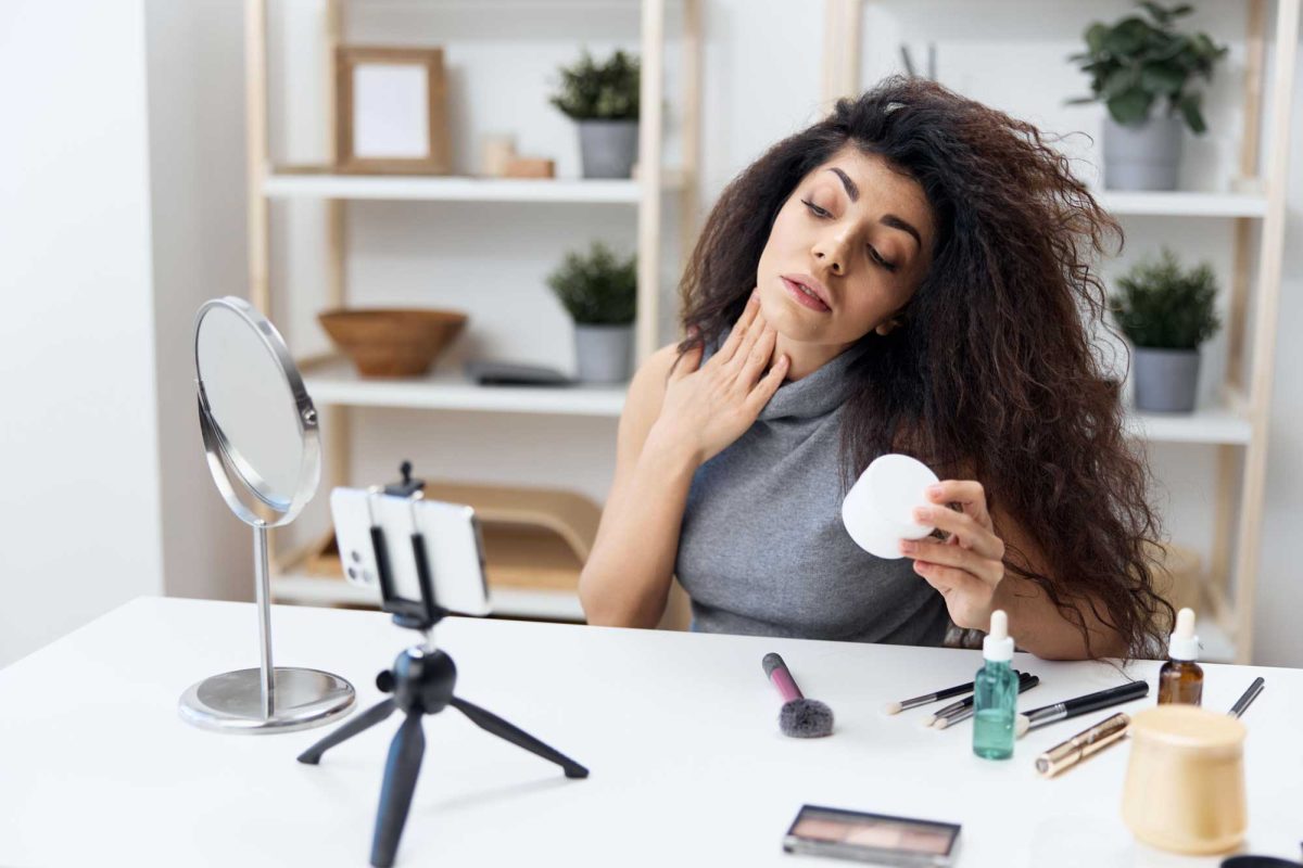 Woman examining neck using mirror, beauty products around