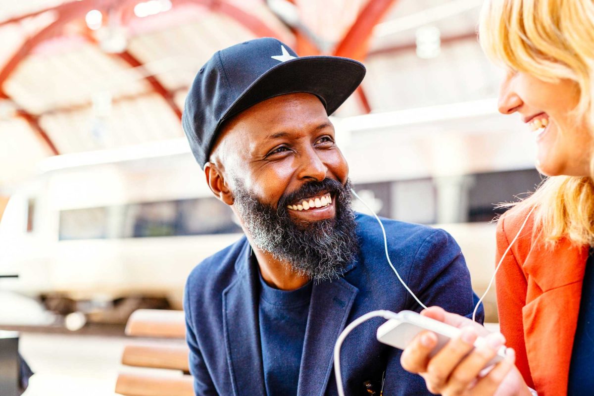 Joyful bearded man sharing music with woman at station