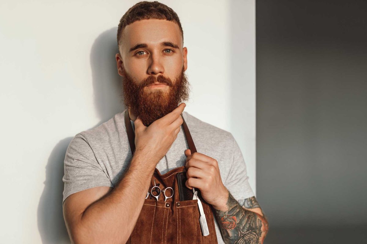 Bearded man holding scissors in sunny studio.