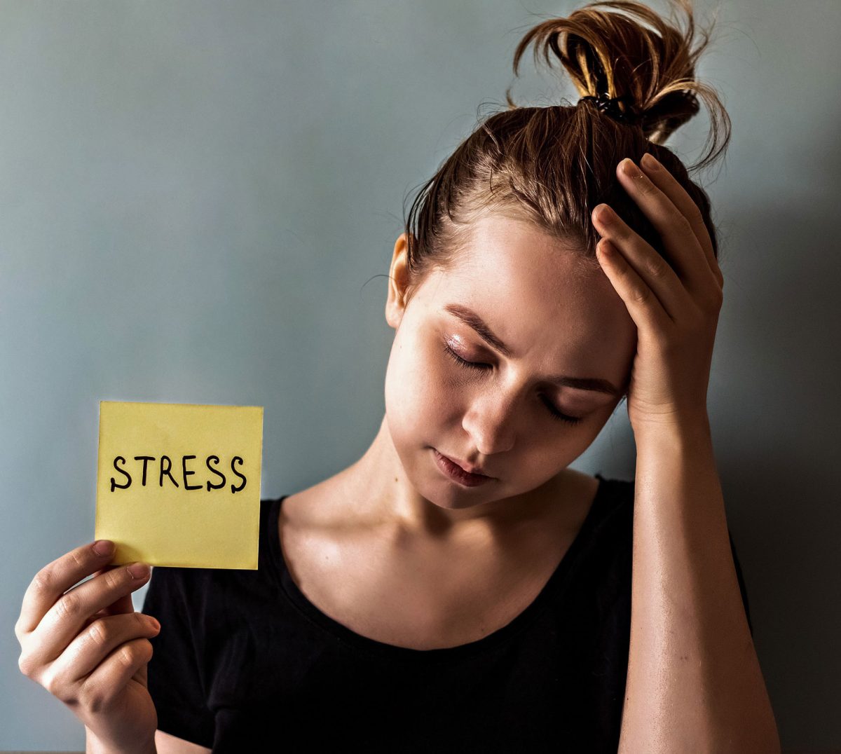 Woman holding 'STRESS' note, looking exhausted