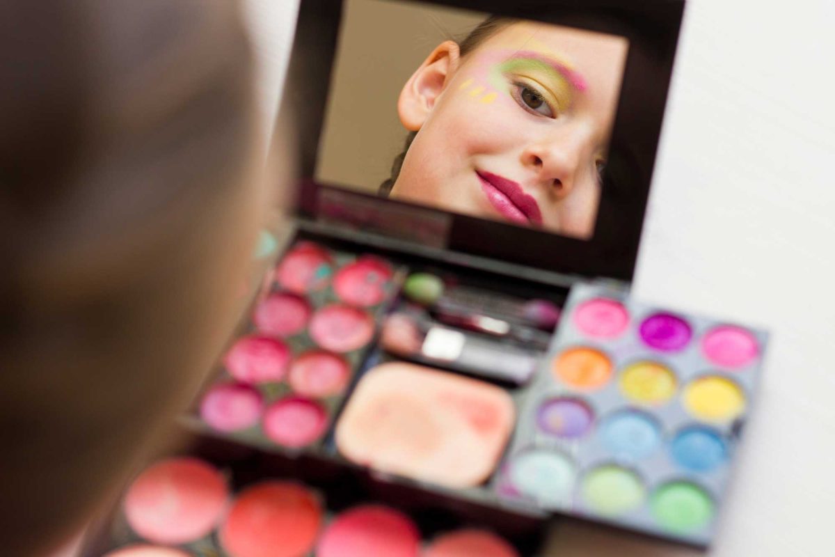 Young girl applying colorful makeup, reflected in mirror